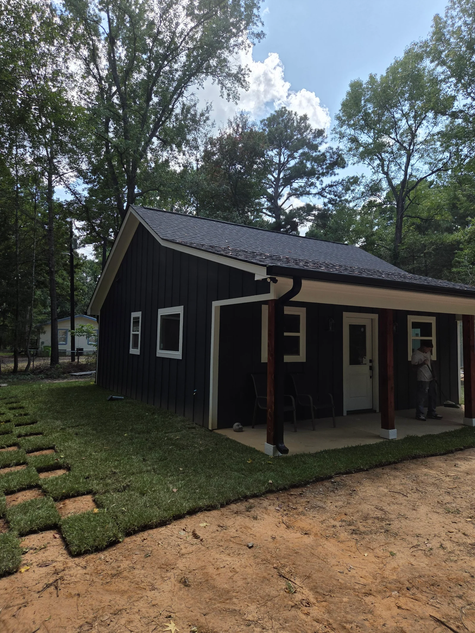 Black board-and-batten cottage with cream trim, gabled roof, covered porch with support posts