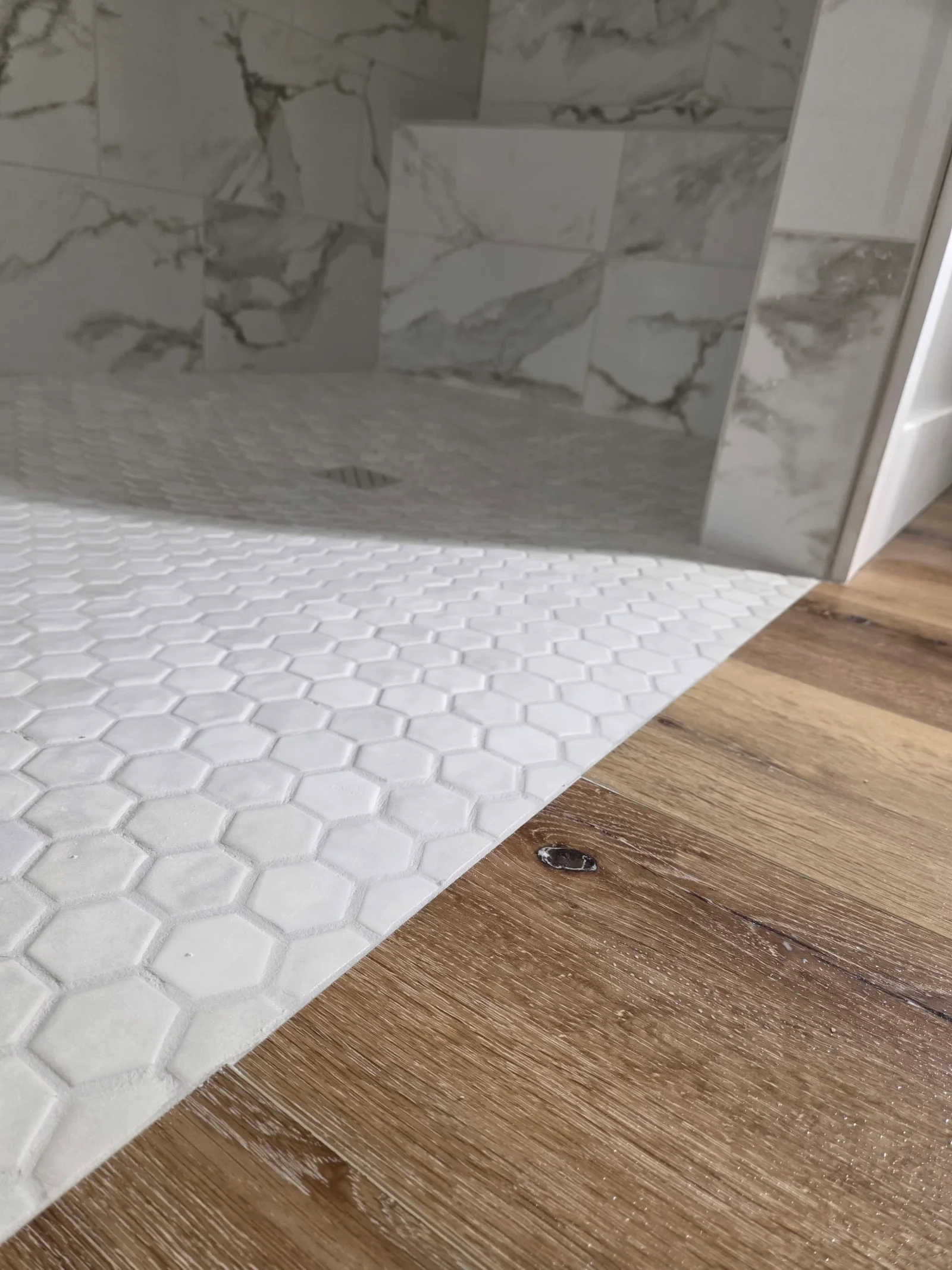 White hexagon tile floor and marble tile shower surround with natural veining in bathroom