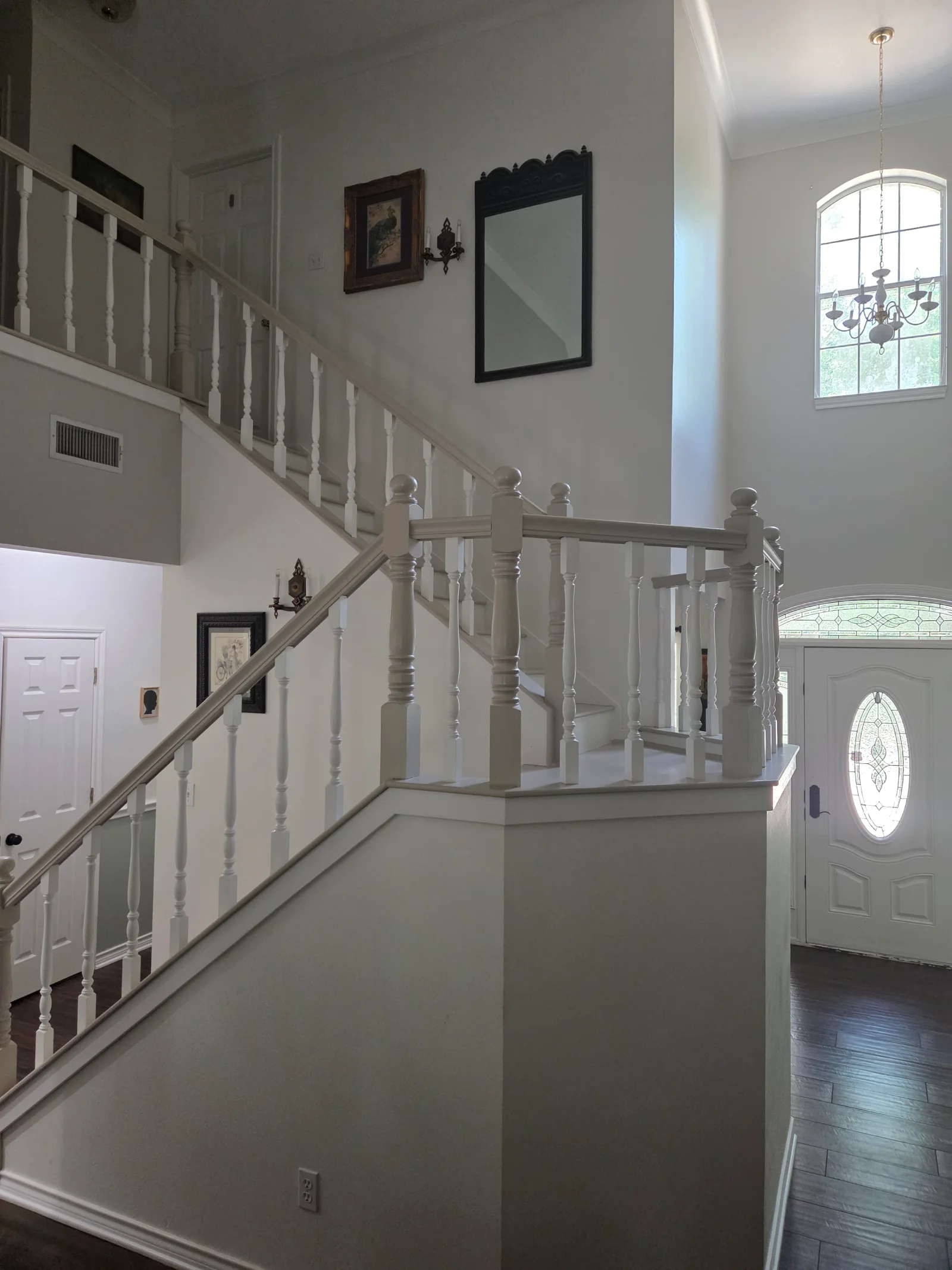 Two-story foyer with gray-white turned-spindle staircase, hardwood floors, and arched entry door