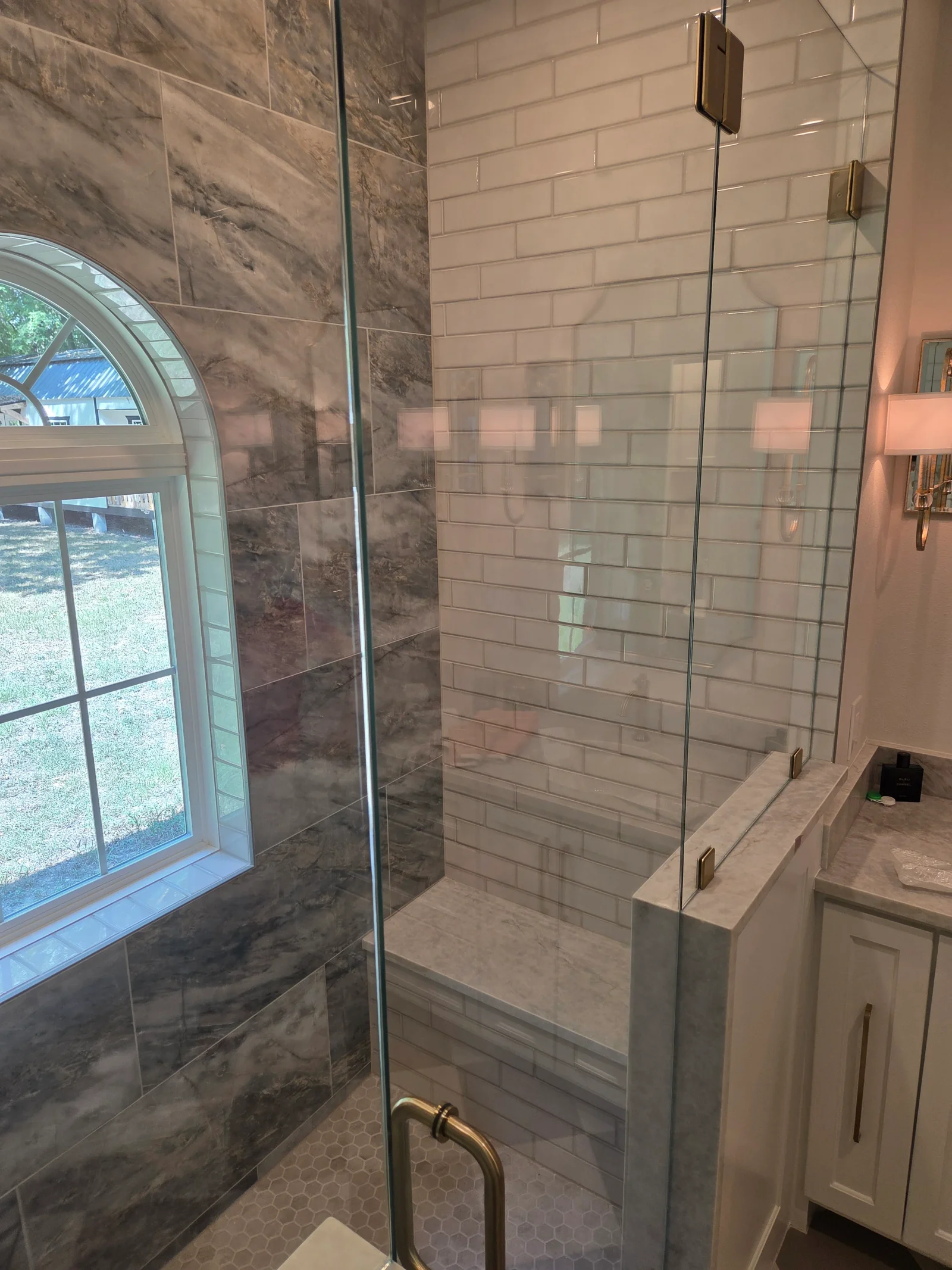 Marble and subway tile walk-in shower with frameless glass door and built-in bench