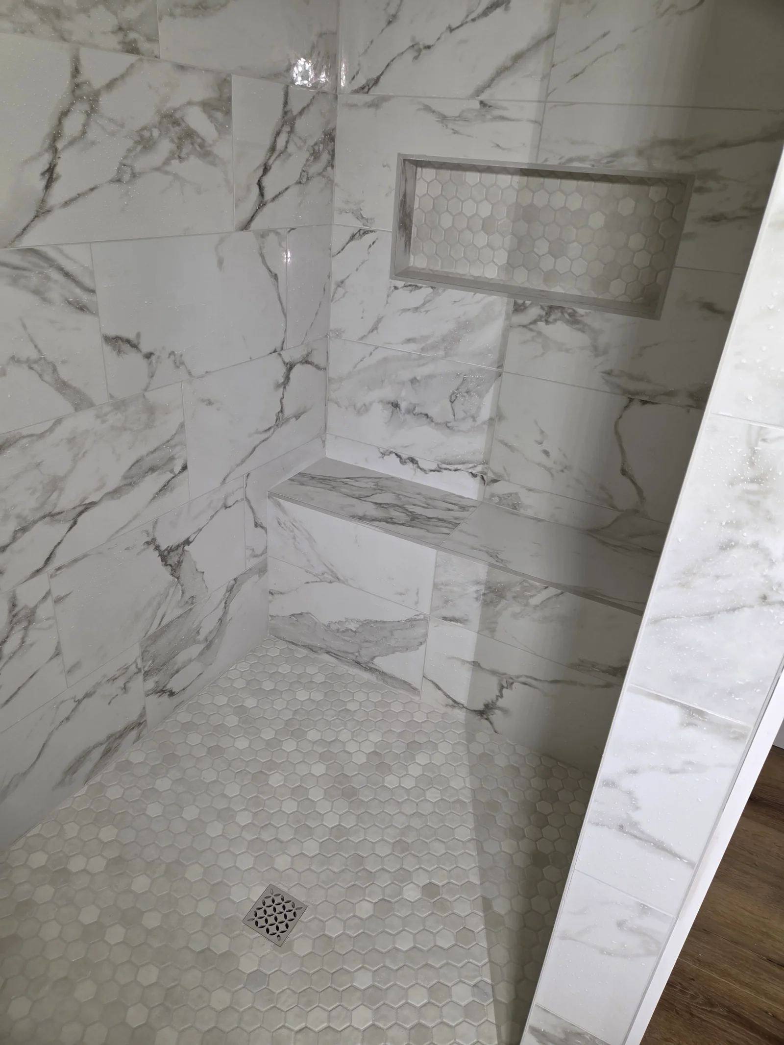 Marble-look porcelain tile shower with hexagonal floor tile and built-in niche