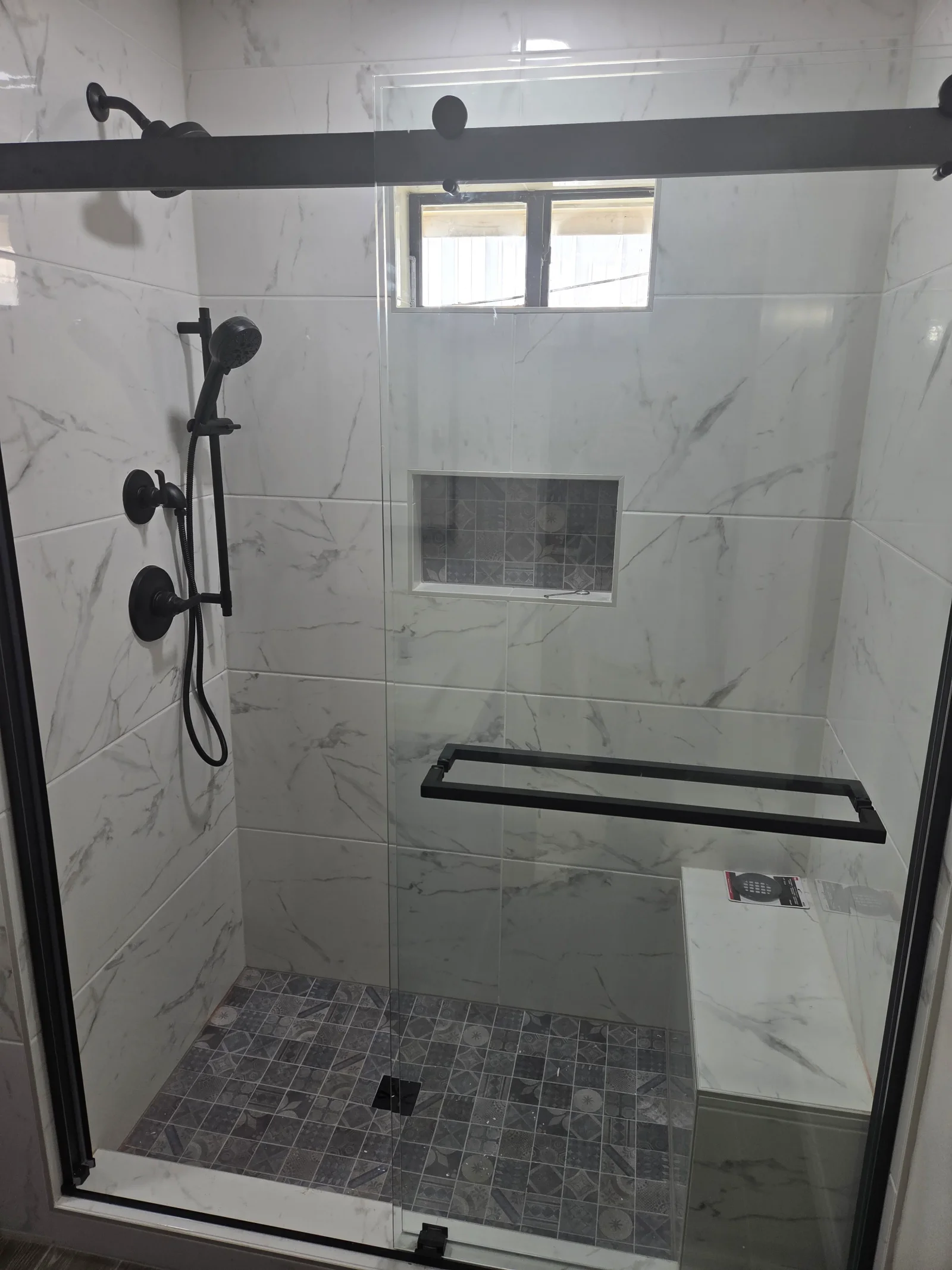 Marble tile shower with frameless glass door, black fixtures, and gray mosaic floor tile