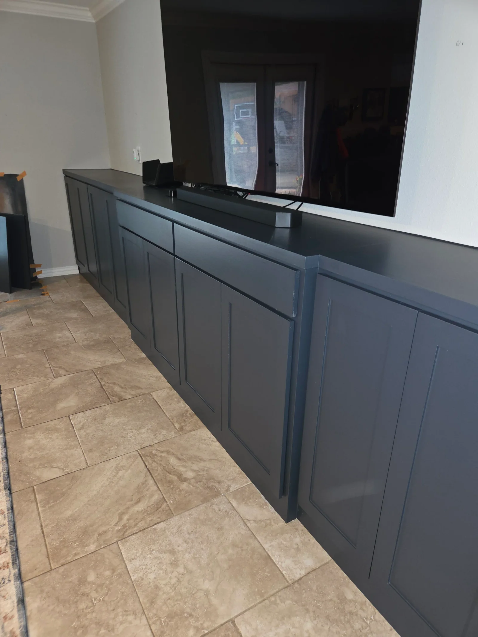 Charcoal gray shaker cabinetry media console with travertine tile flooring and mounted TV