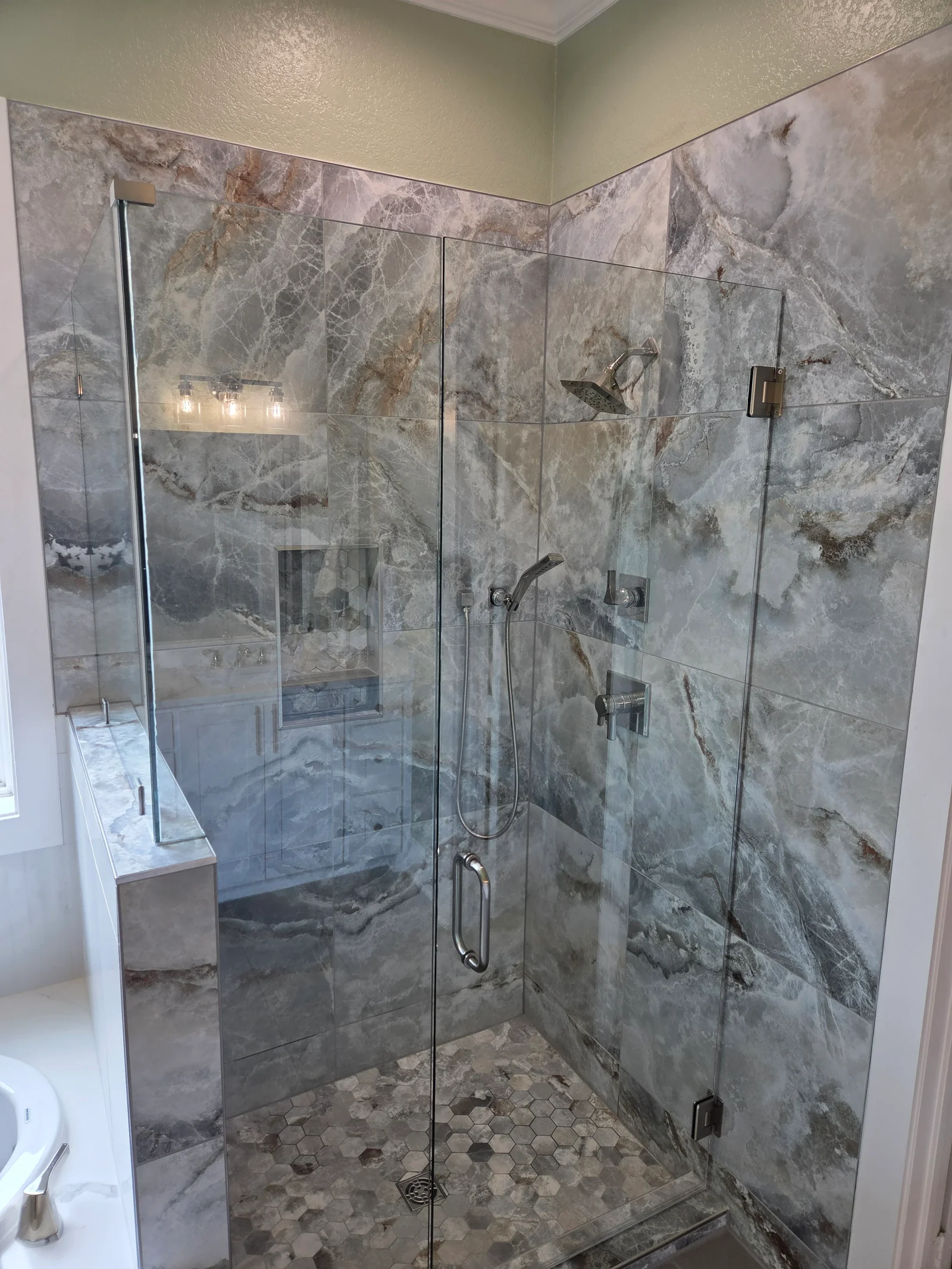 Marble tile shower with frameless glass doors, rainfall showerhead, and hexagonal floor tile