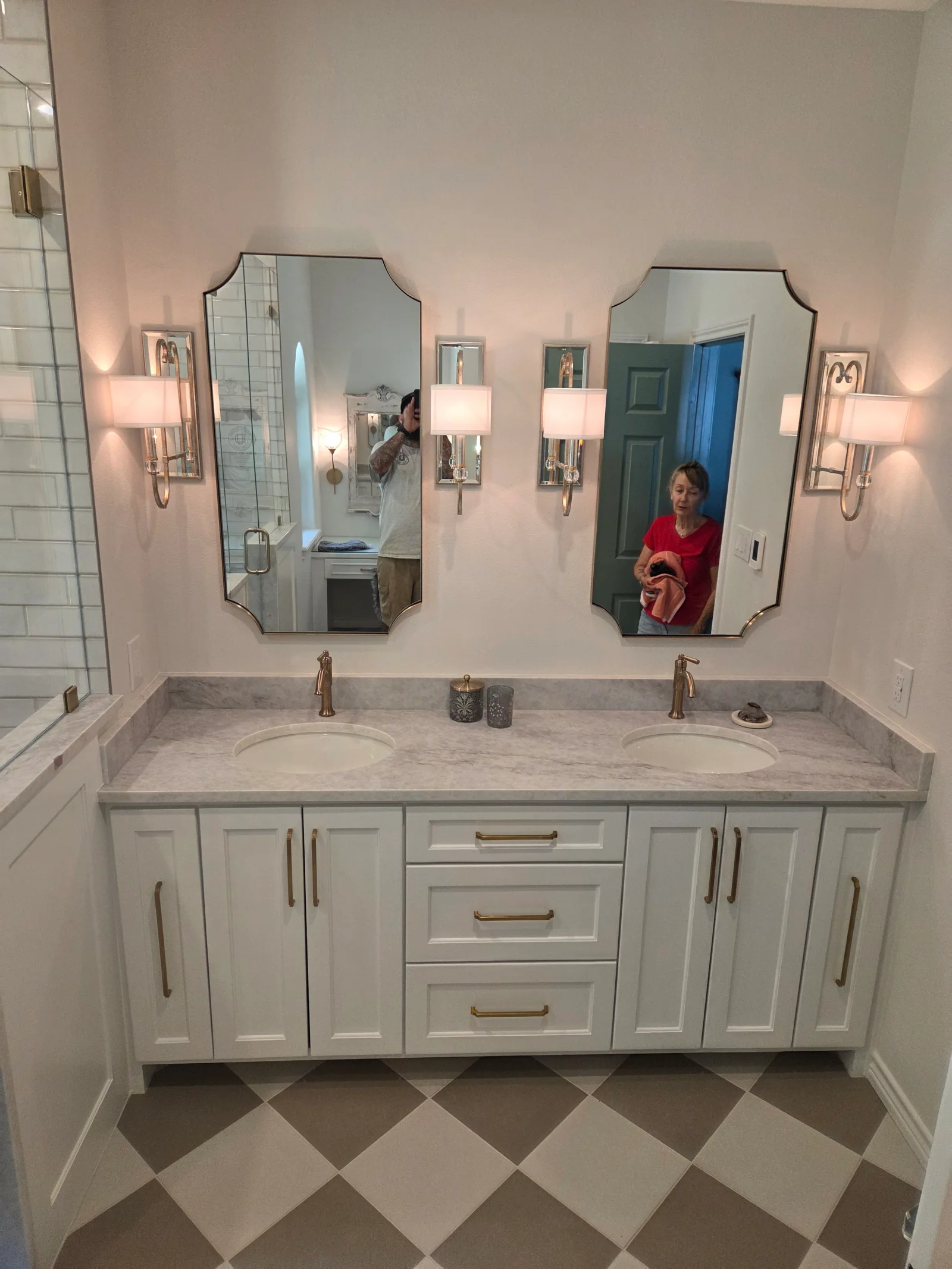 White cabinetry vanity with gray marble countertop, dual sinks, arched mirrors, and geometric tile flooring