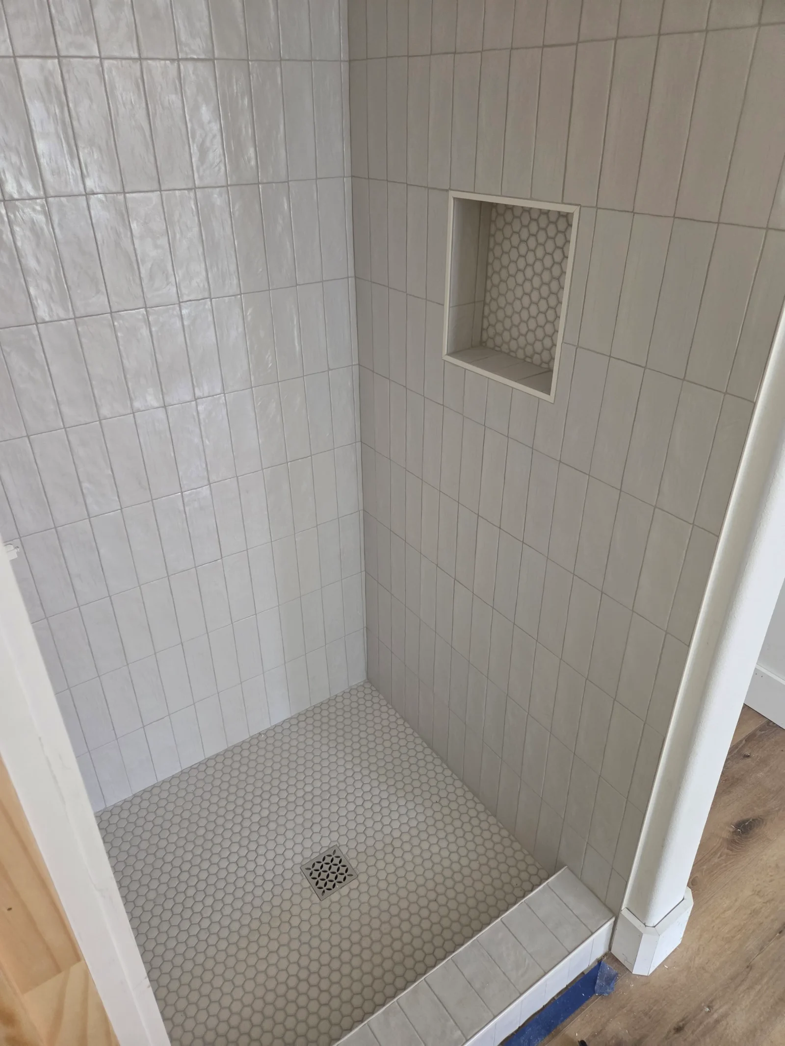White subway tile shower walls with gray hexagon mosaic floor and recessed niche