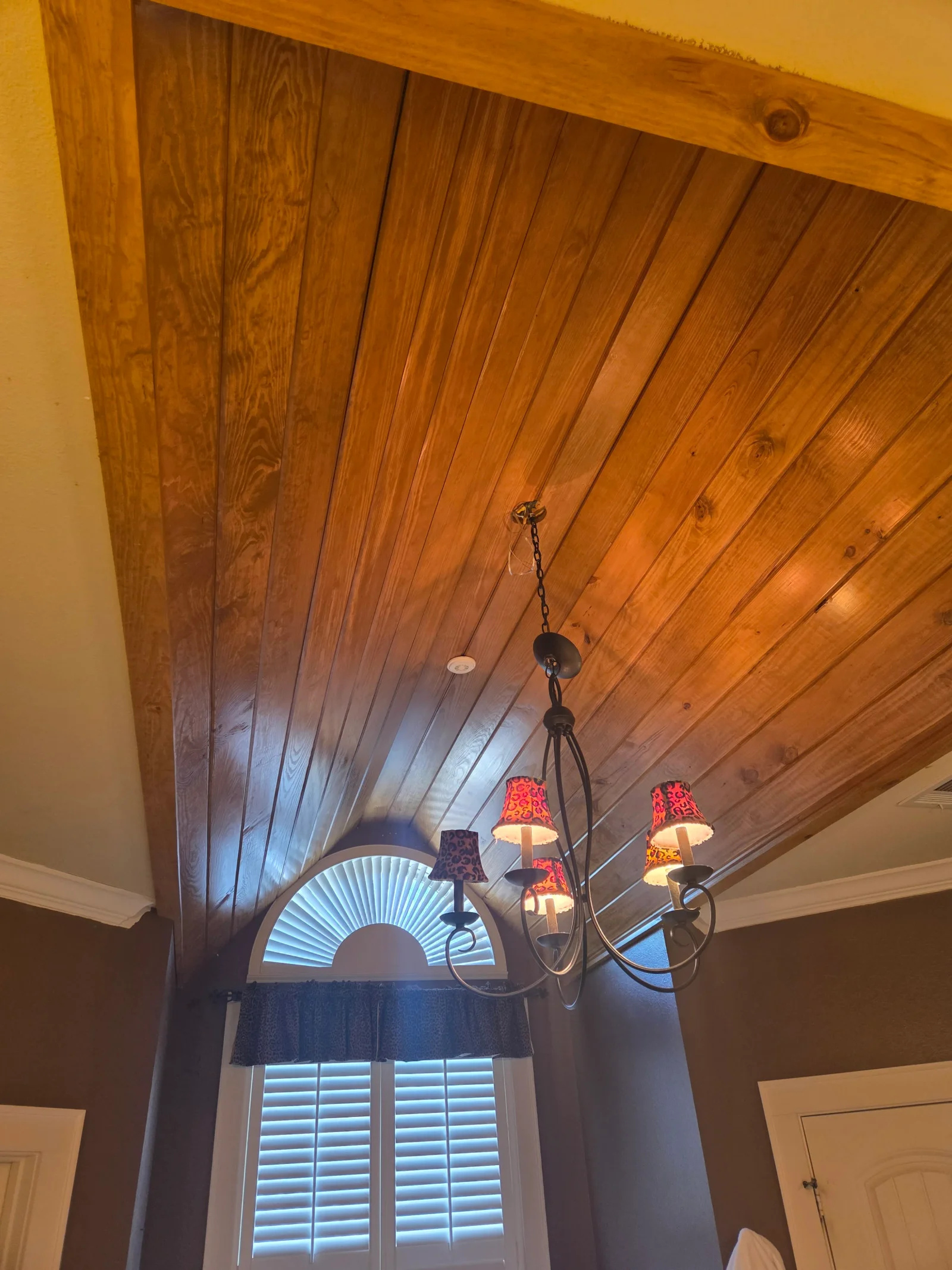 Angled tongue-and-groove wood ceiling with wrought-iron chandelier and red fabric shades