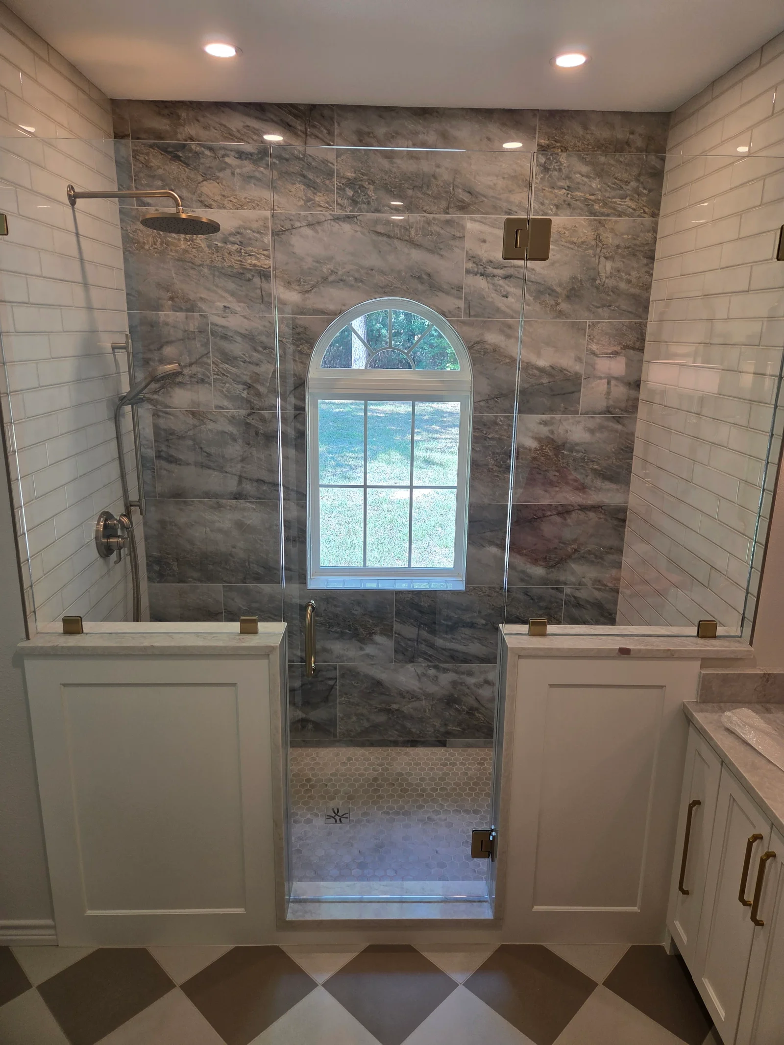 Marble tile shower with frameless glass enclosure, white subway tile walls, and geometric floor pattern