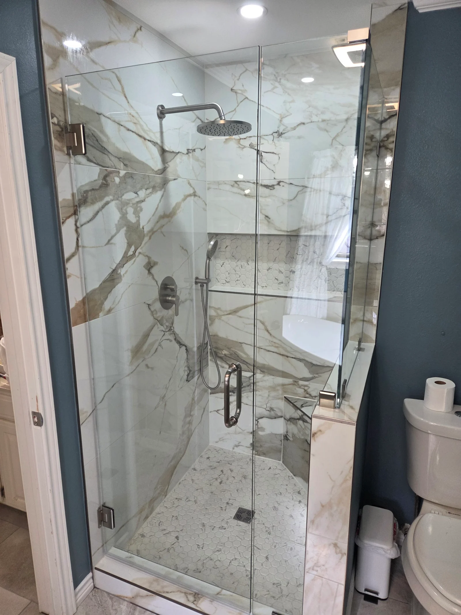 Frameless glass shower with marble tile walls and floor, chrome fixtures, and rainfall showerhead