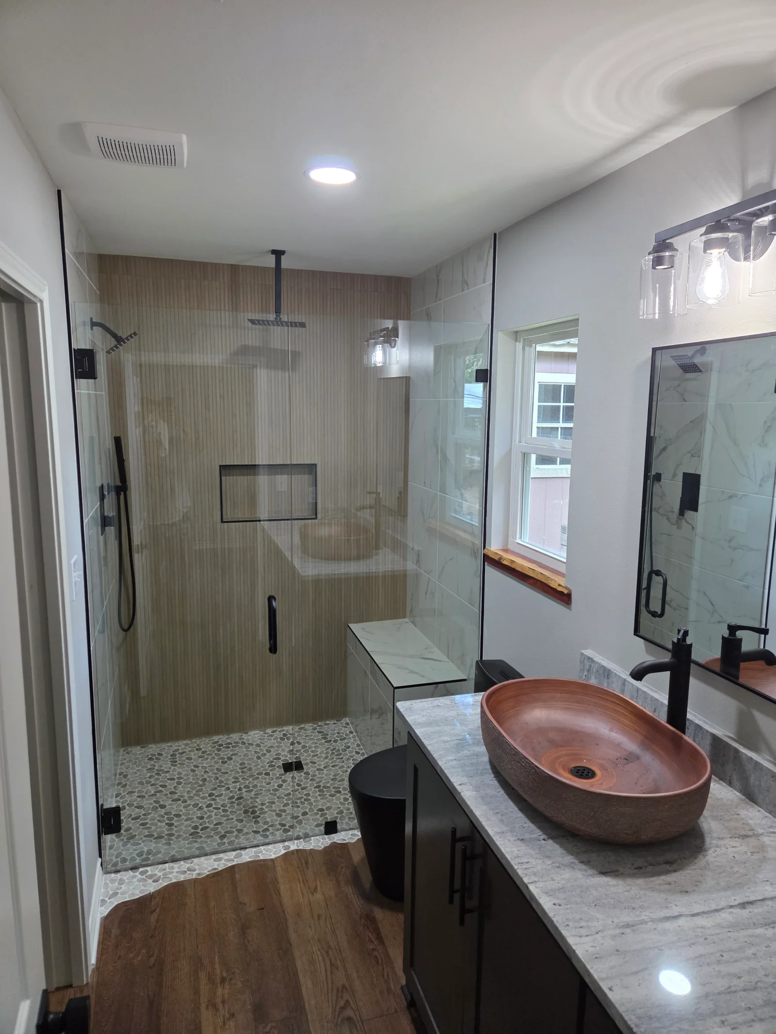 Frameless glass shower, marble counters, copper vessel sink, black fixtures, pebble tile floor