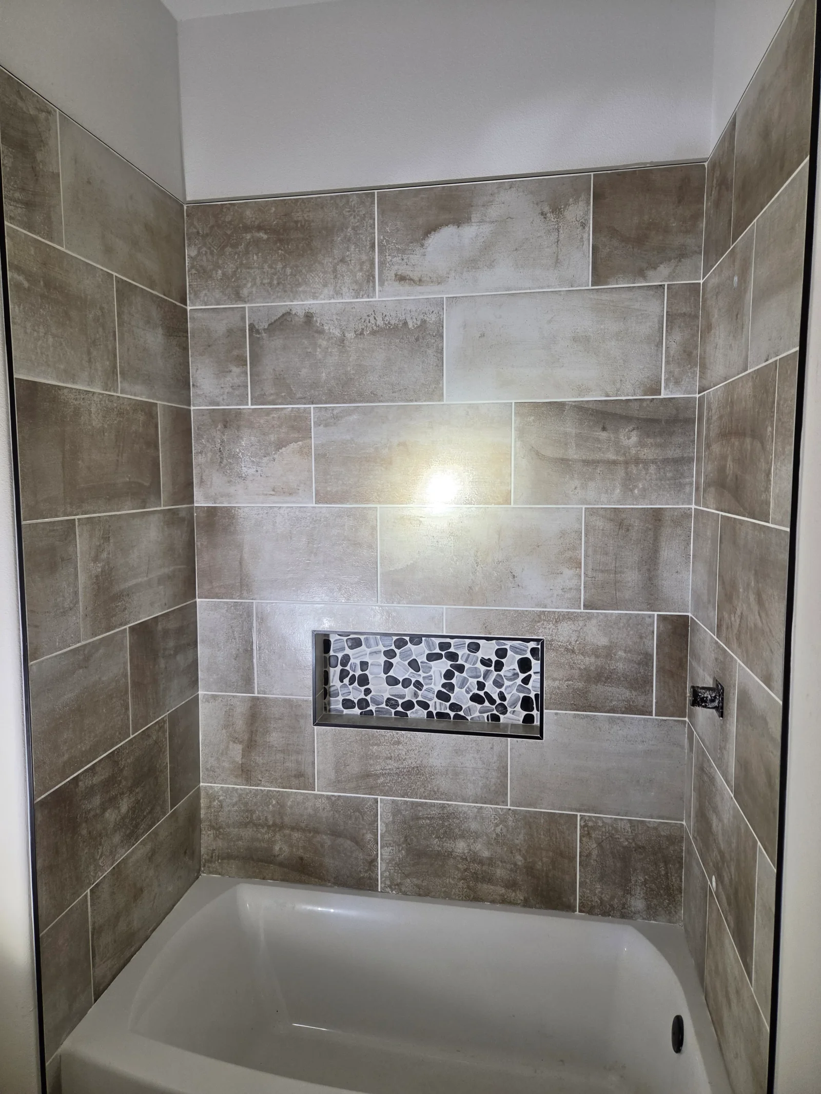 Gray porcelain tile shower surround with recessed niche and pebble mosaic accent
