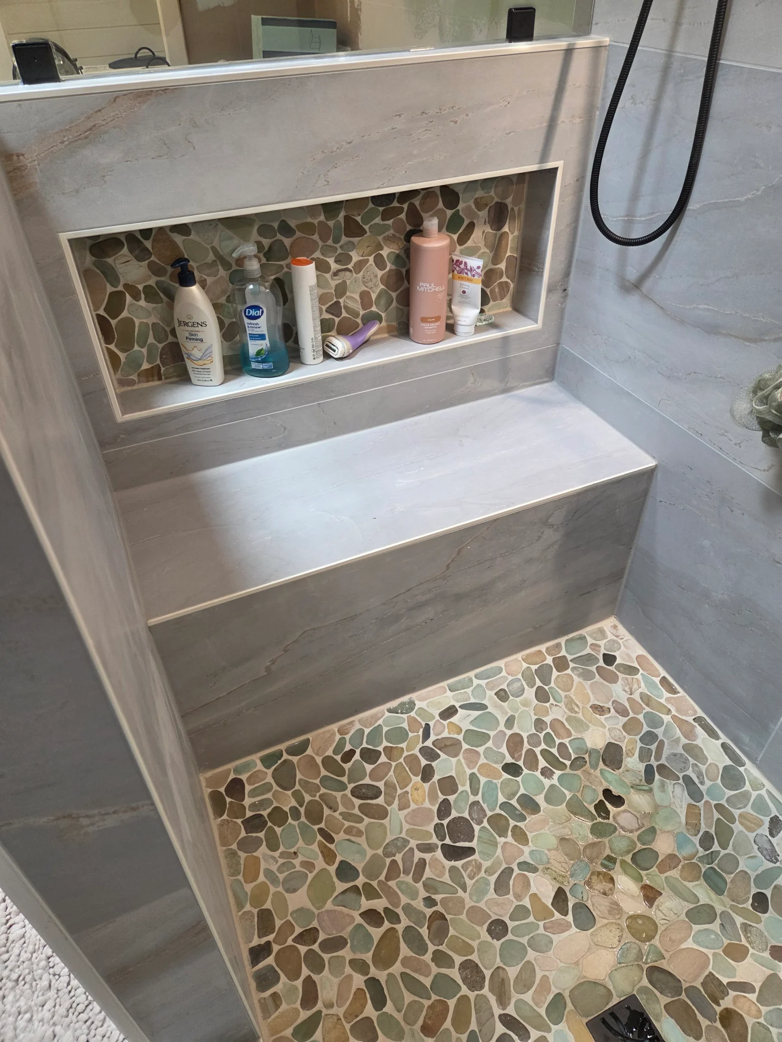 Recessed bathroom niche with pebble tile backing, white shelf, and matching pebble tile floor