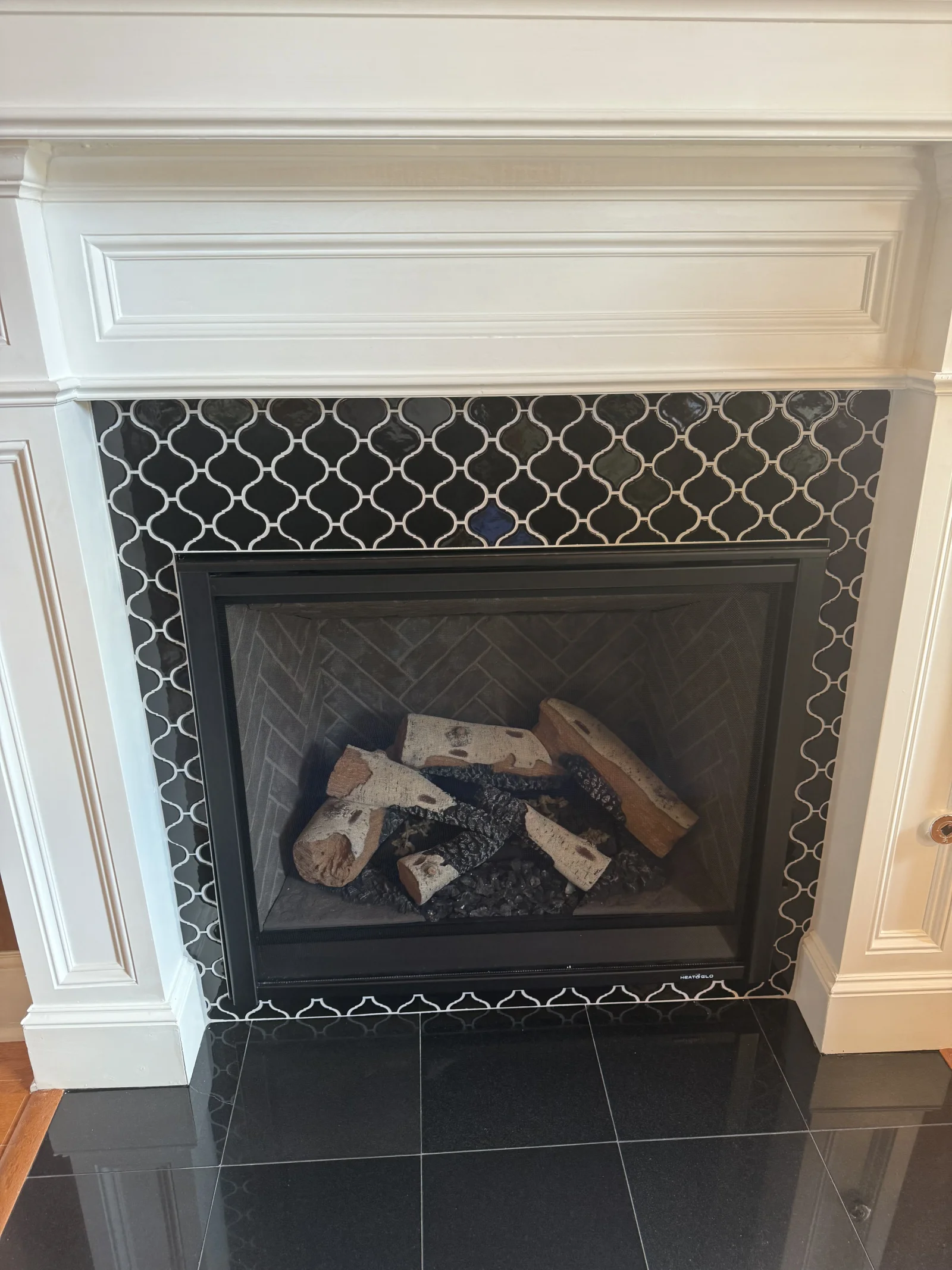 Fireplace with quatrefoil patterned charcoal tile surround, black slate hearth, and white painted mantel trim