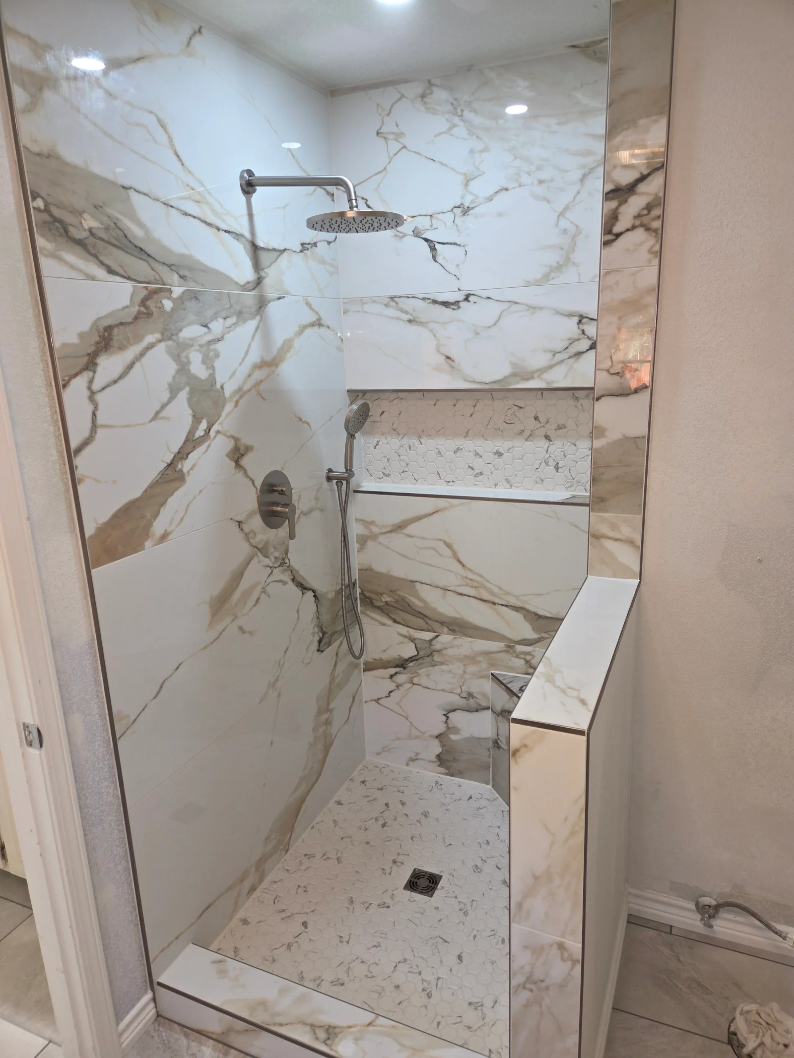 Marble tile shower with frameless glass door, rainfall showerhead, and bench seating