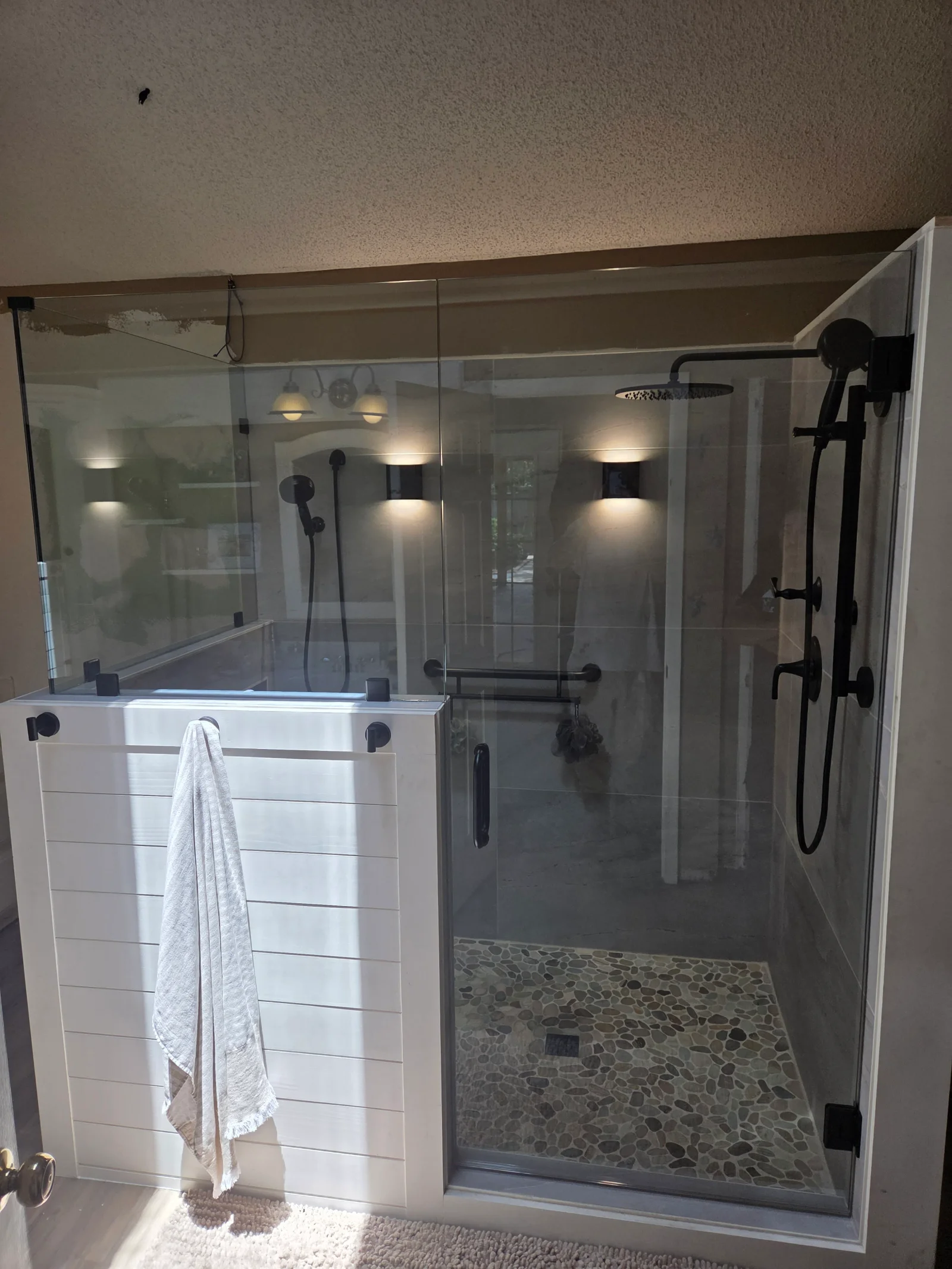 Frameless glass shower enclosure with black hardware, pebble floor, and recessed lighting