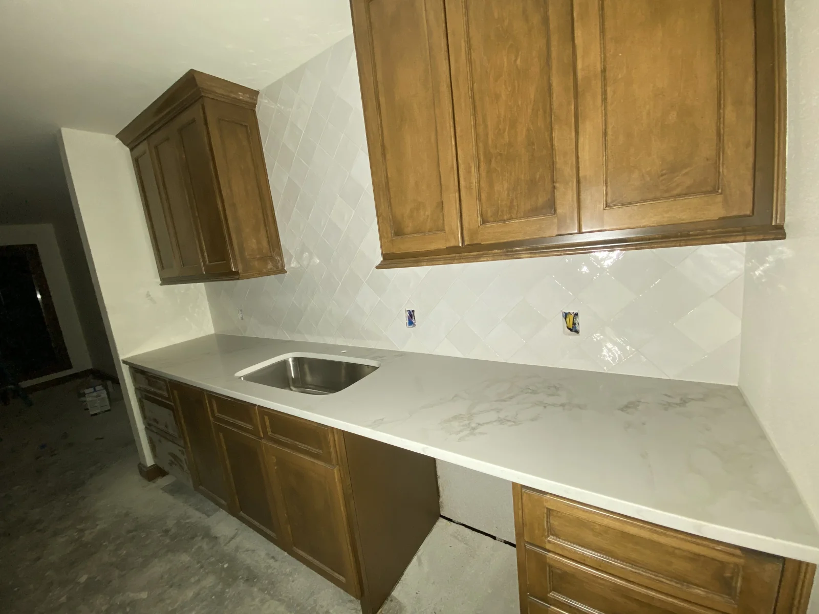 White quartz countertops with herringbone tile backsplash and wood cabinetry kitchen installation