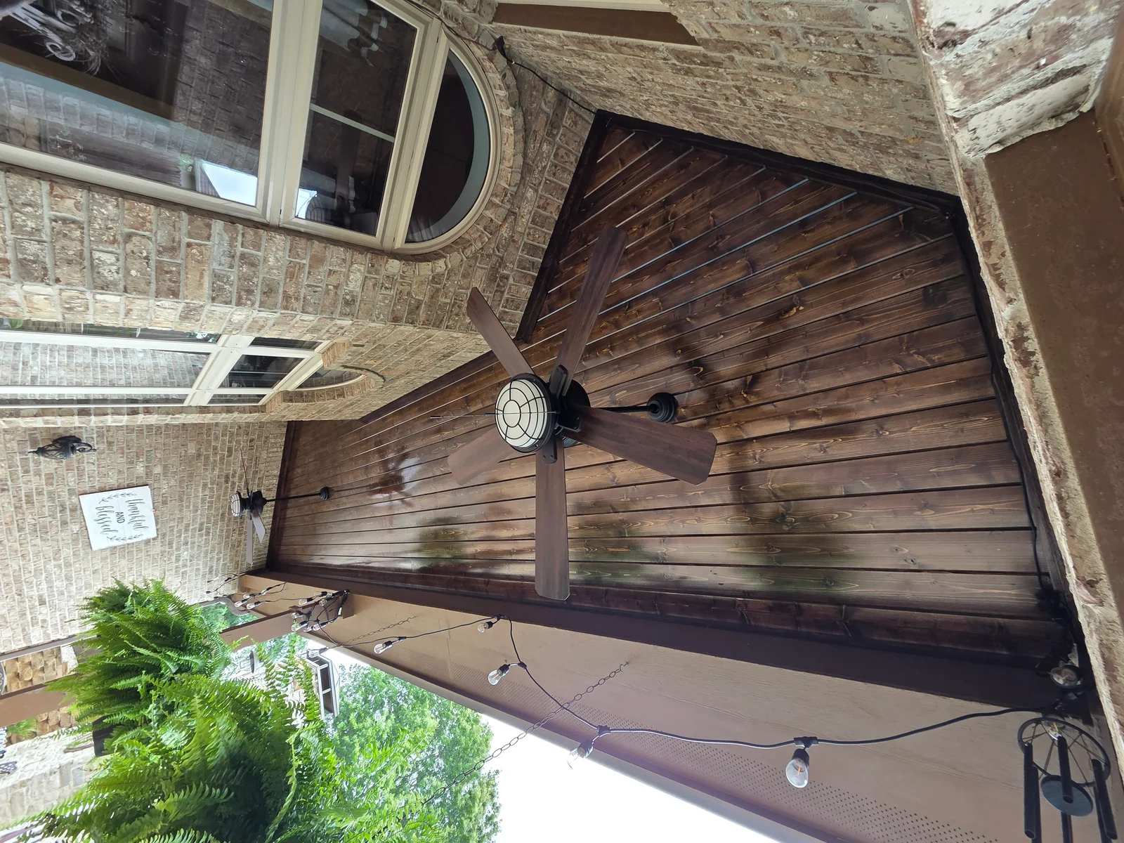 Dark stained wood plank ceiling with ceiling fan in covered patio area