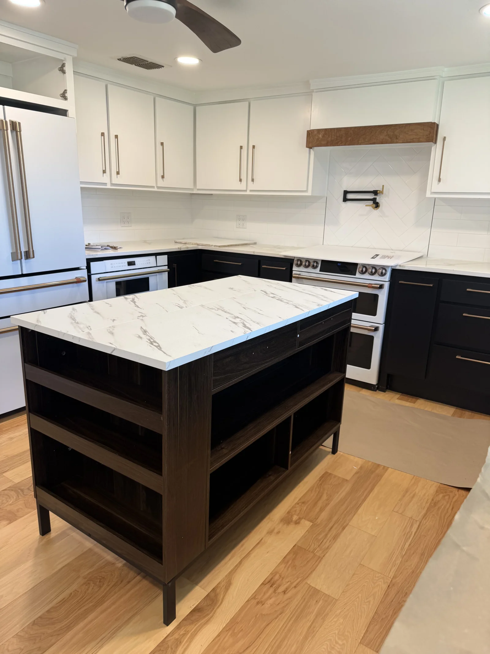 Modern kitchen with white upper cabinets, dark lower cabinets, marble quartz island, stainless appliances, and wood flooring