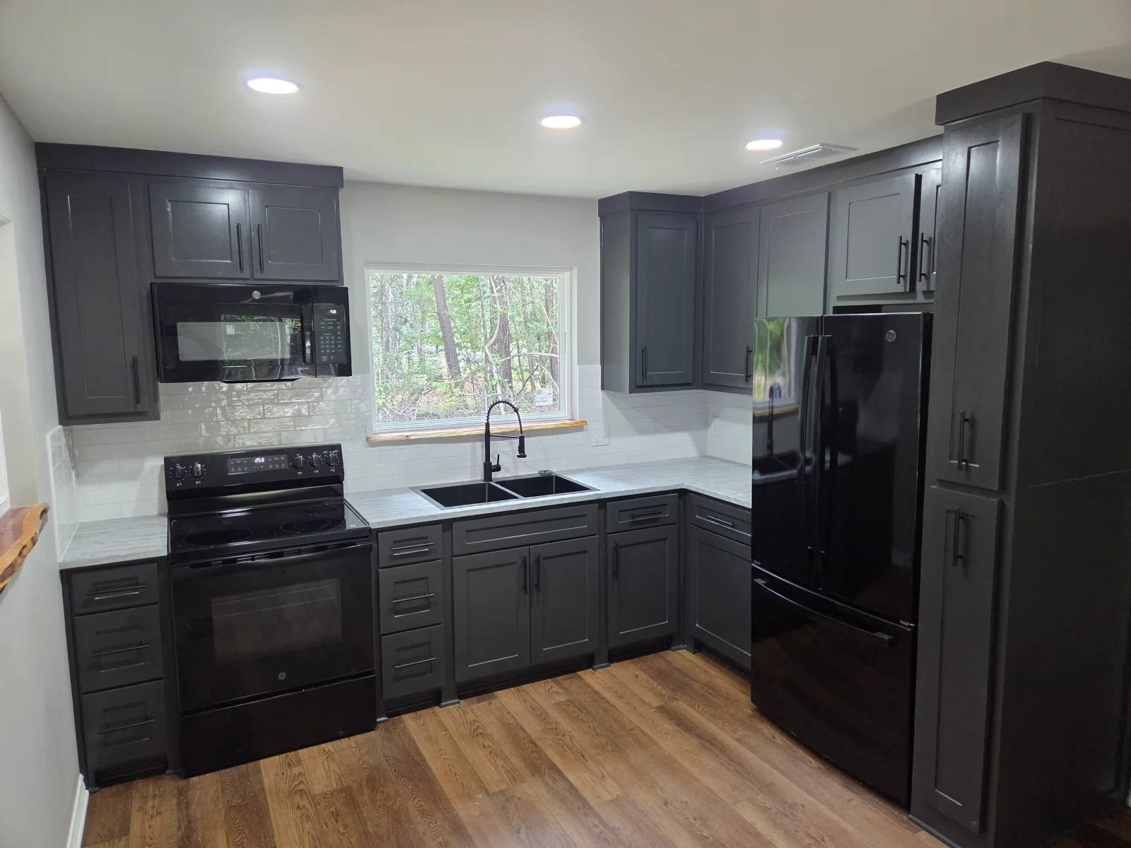 Dark gray kitchen cabinets, white quartz counters, subway tile backsplash, black stainless appliances