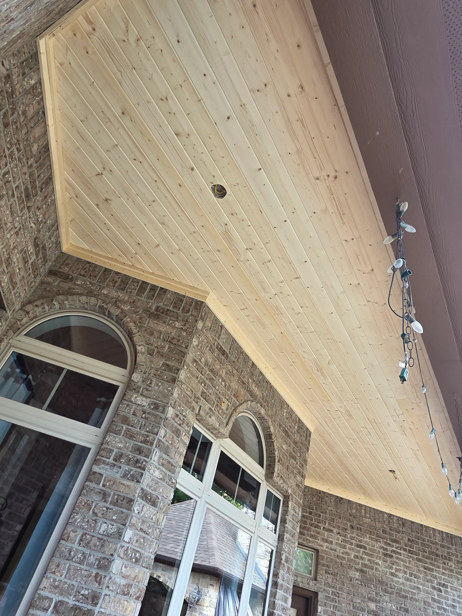Light wood tongue and groove soffit with diagonal planking installed on brick exterior